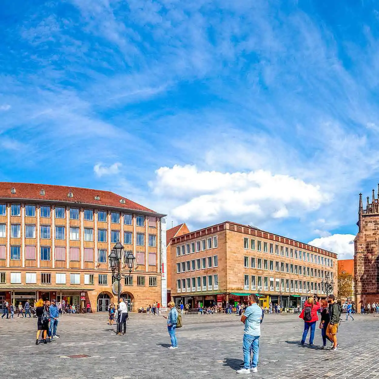 Belebter Stadtplatz bei Tageslicht Belebter städtischer Platz mit Menschen, gepflastertem Boden und Gebäuden bei blauem Himmel.