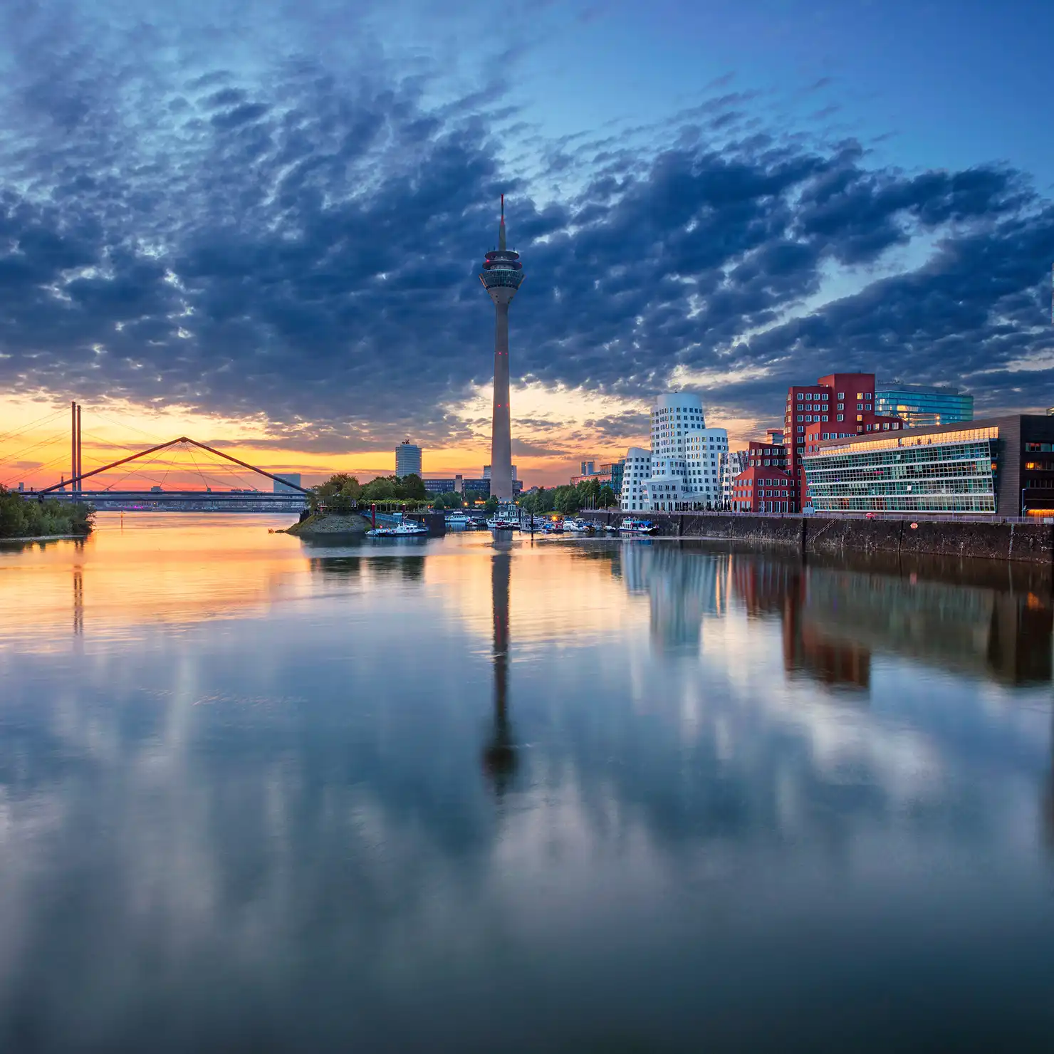 Düsseldorfer Skyline bei Sonnenuntergang Skyline von Düsseldorf mit dem Rheinturm und den modernen Gebäuden des MedienHafens im Vordergrund, reflektiert in ruhigem Wasser bei Sonnenuntergang