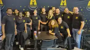 Zwölf Personen in schwarzen Matagot-Shirts vor Matagot & Friends-Hintergrund an Tisch mit Spielkarten.